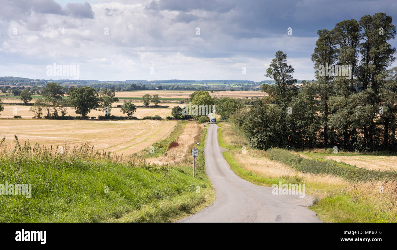 A single track country lane runs through fields of crops and pasture at Tansor Wold near Oundle in Northamptonshire's Nene Valley. Stock Photo