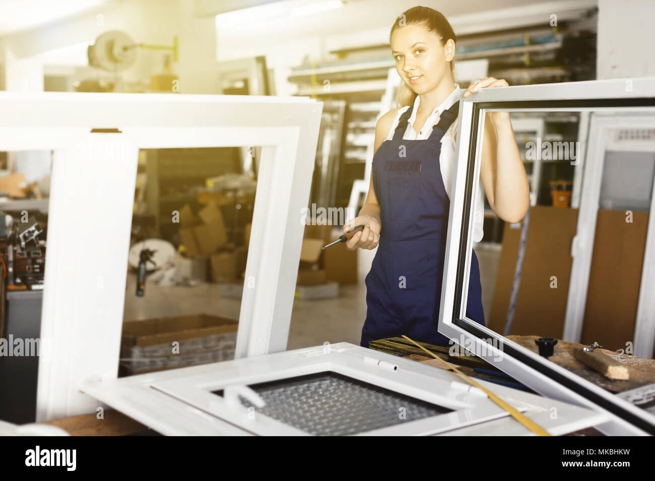 Diligent  positive  workwoman assembling PVC window in workshop with manual tools Stock Photo