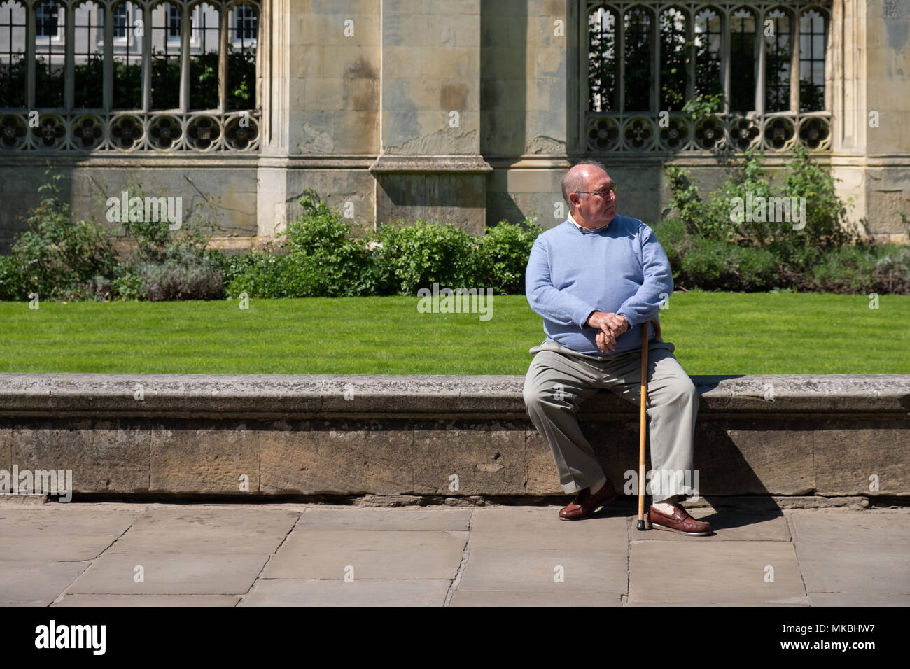 Obese man in a blue jumper sitting on the wall outside Kingâ€™s College Cambridge. Stock Photo