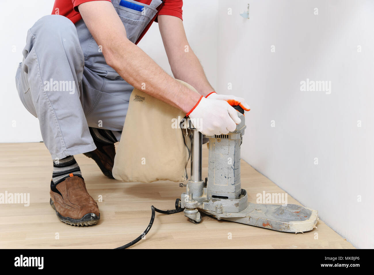 Worker polishing hardwood parquet floor with grinding machine Stock