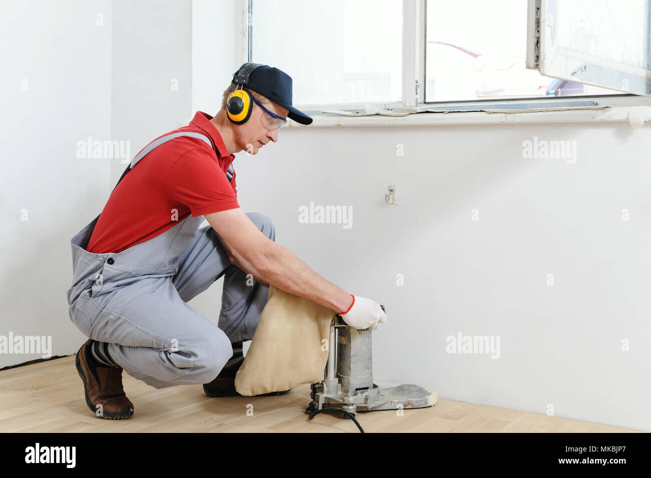 Worker polishing hardwood parquet floor with grinding machine Stock