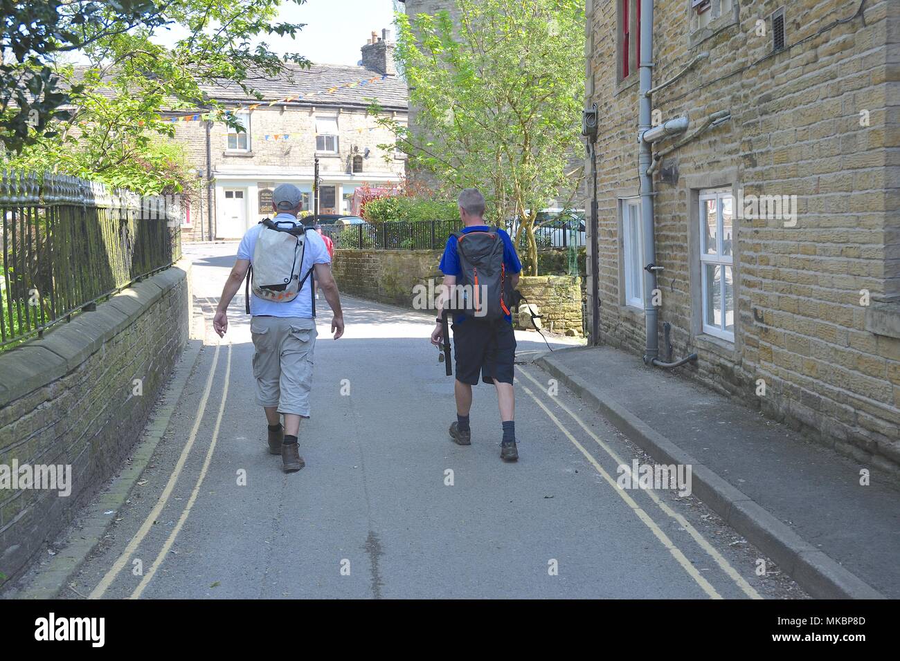 Two men in hiking gear walk through Hayfield Village,  Derbyshire Stock Photo