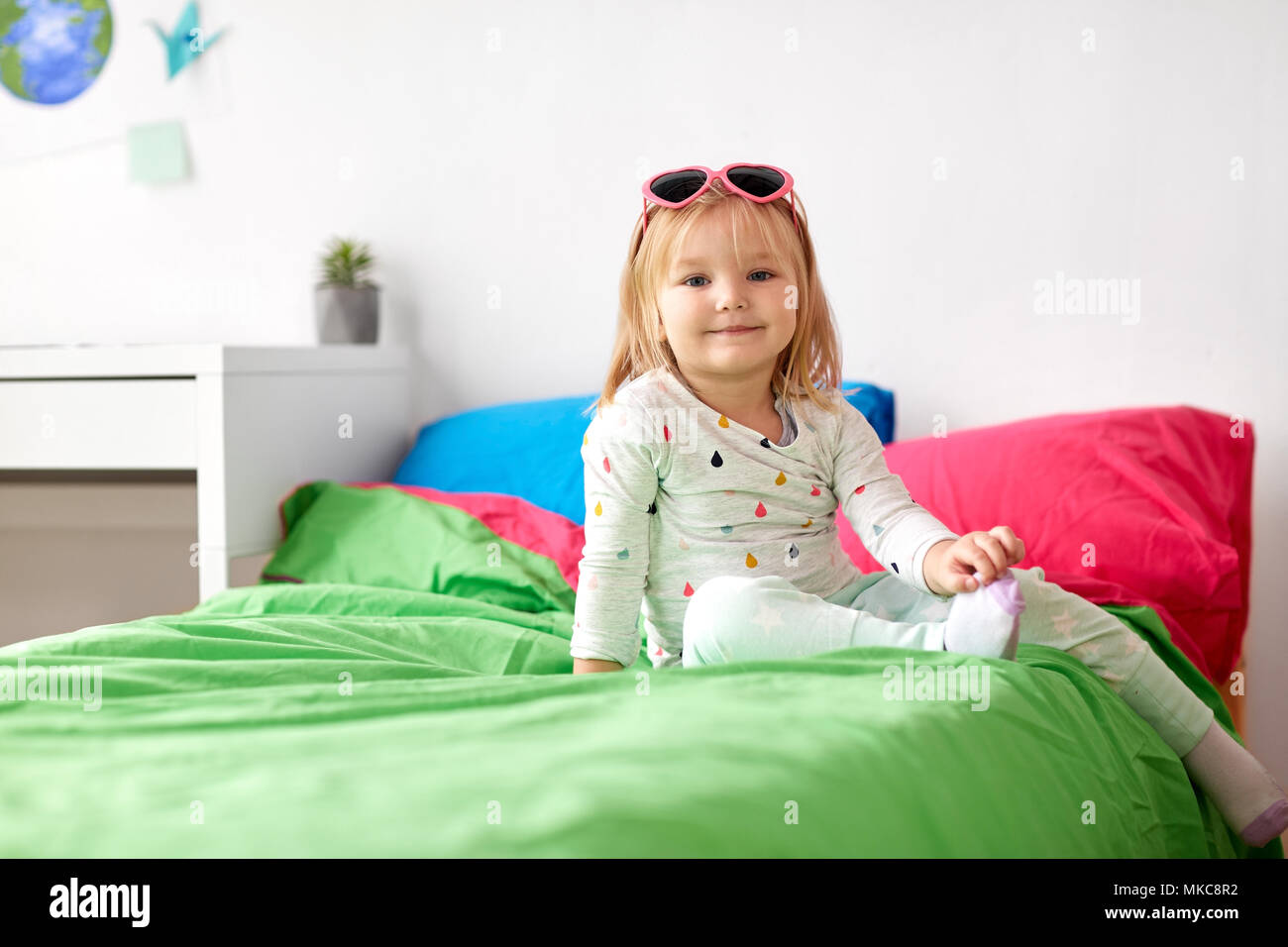 smiling little girl with sunglasses on bed at home Stock Photo Alamy