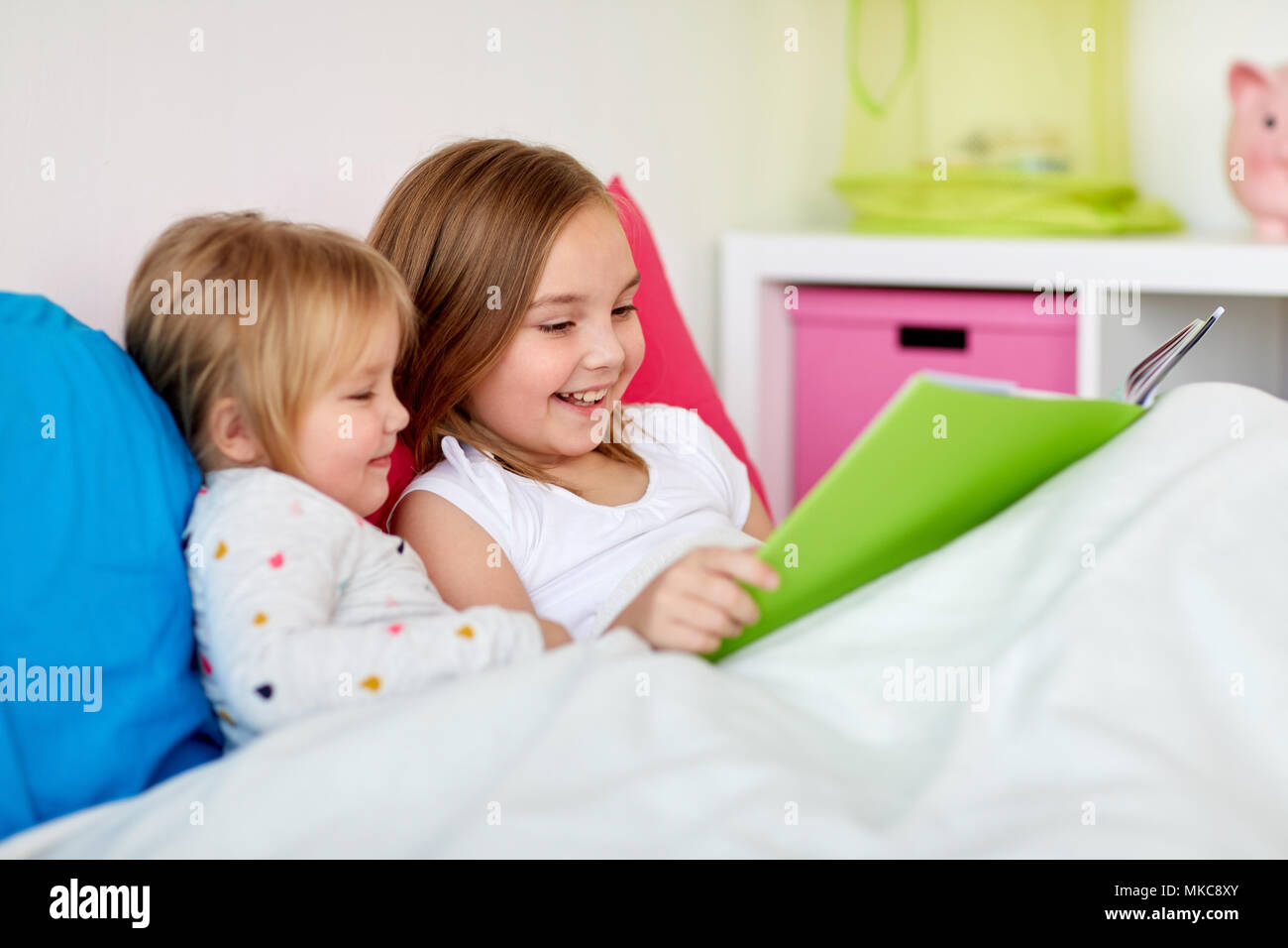 little girls or sisters reading book in bed Stock Photo