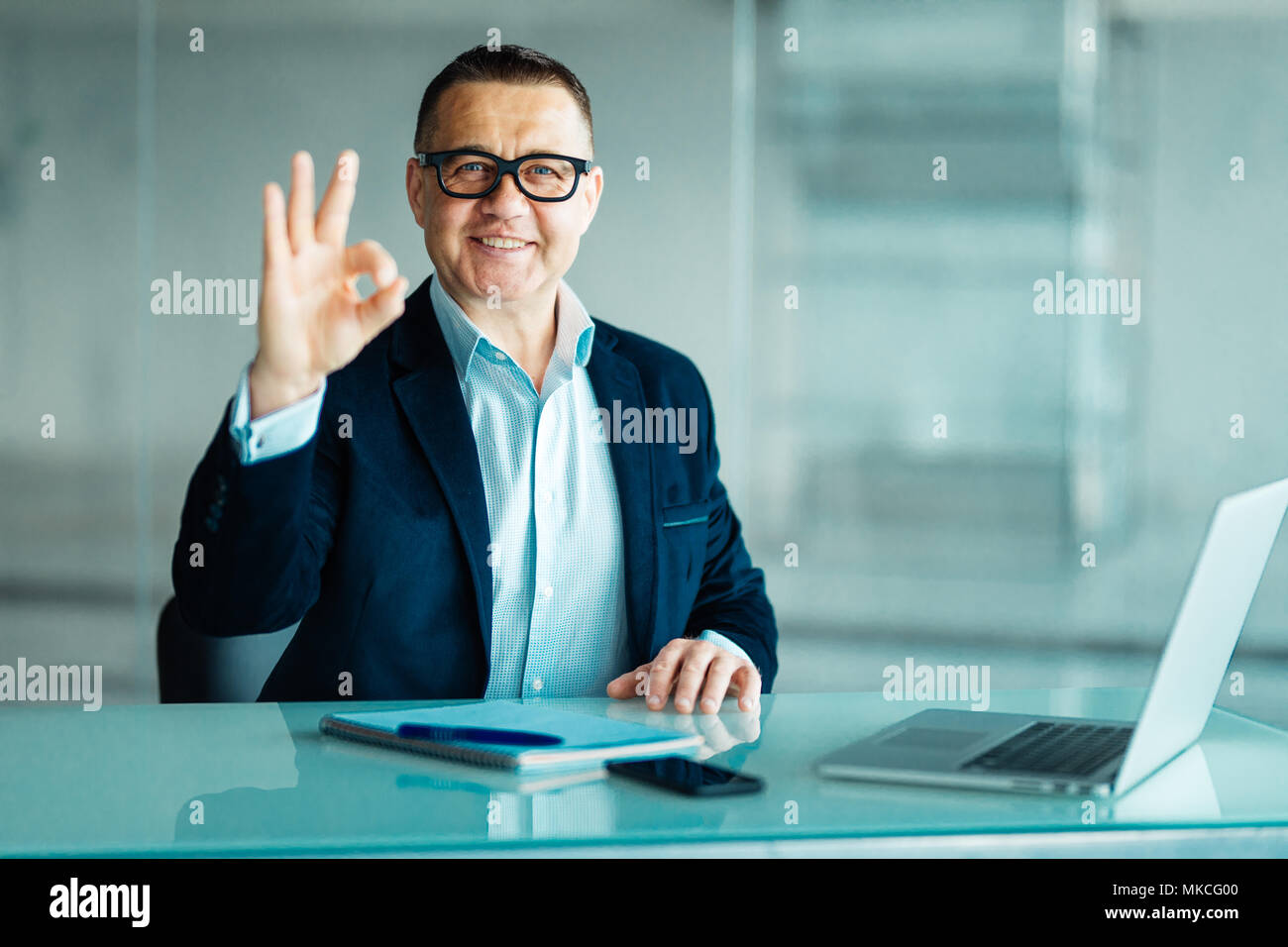 Senior man working on laptop computer with okay sign in office Stock Photo