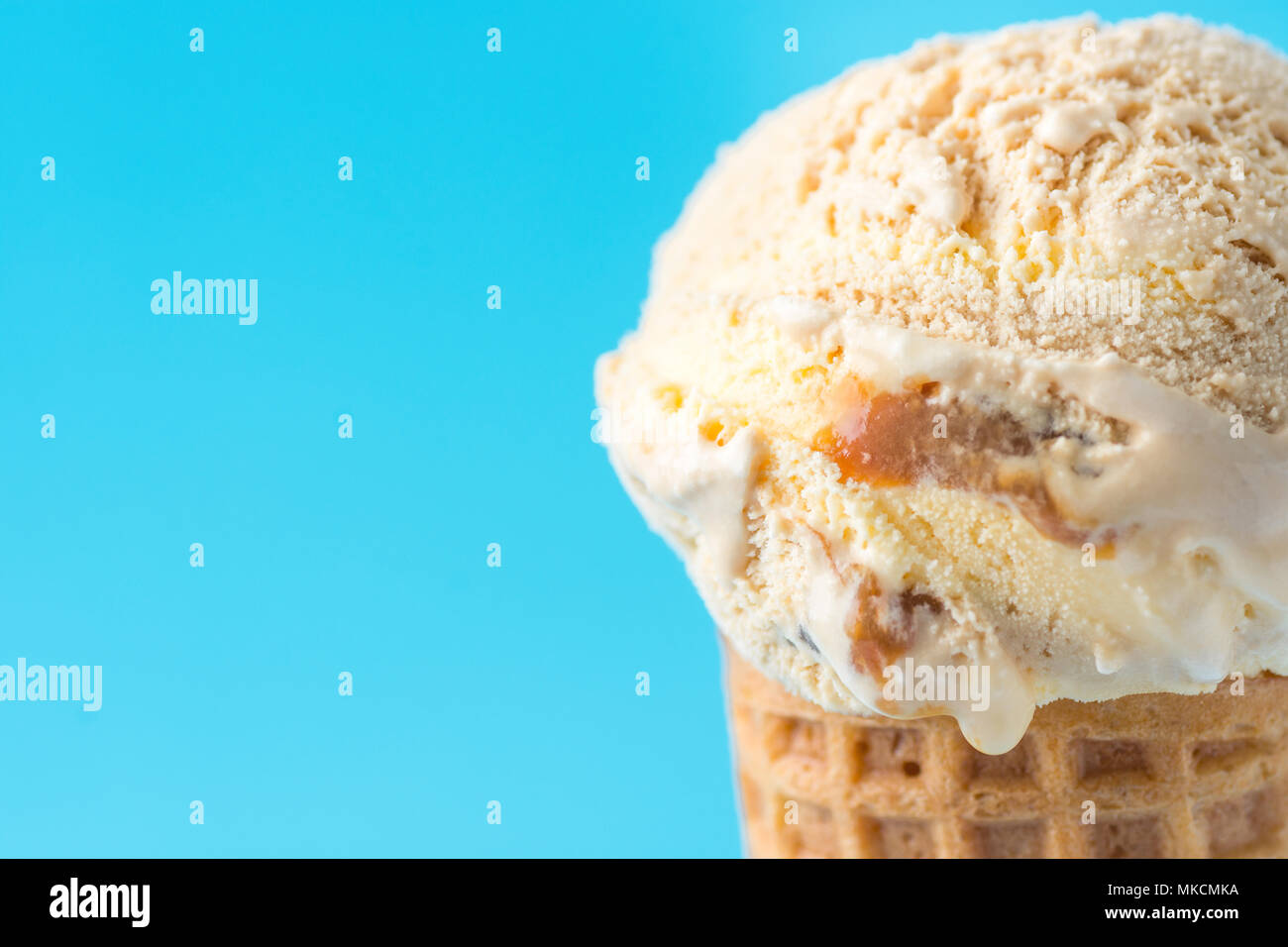 Scoop of Delicious Melting Salted Caramel Toffee Vanilla Ice Cream in Waffle Cone on Blue Background. Summer Sweets Sugar Addiction Indulgence Concept Stock Photo