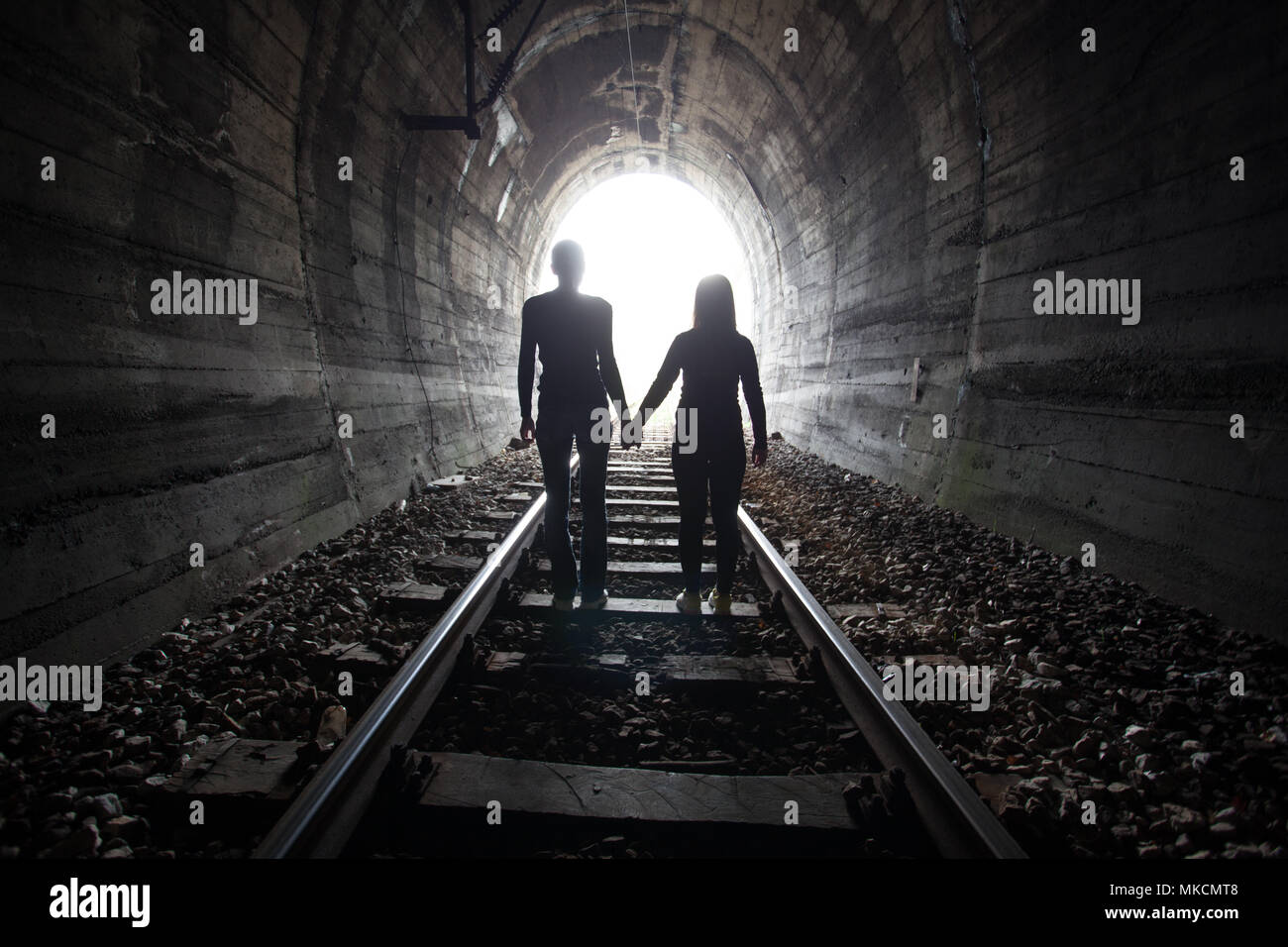 Couple walking hand in hand along the track through a railway tunnel ...