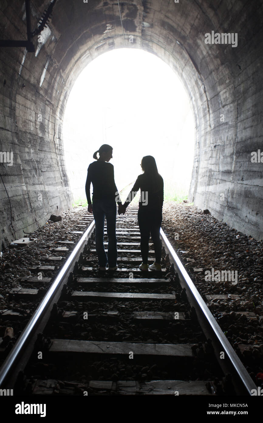 Couple walking hand in hand along the track through a railway tunnel ...