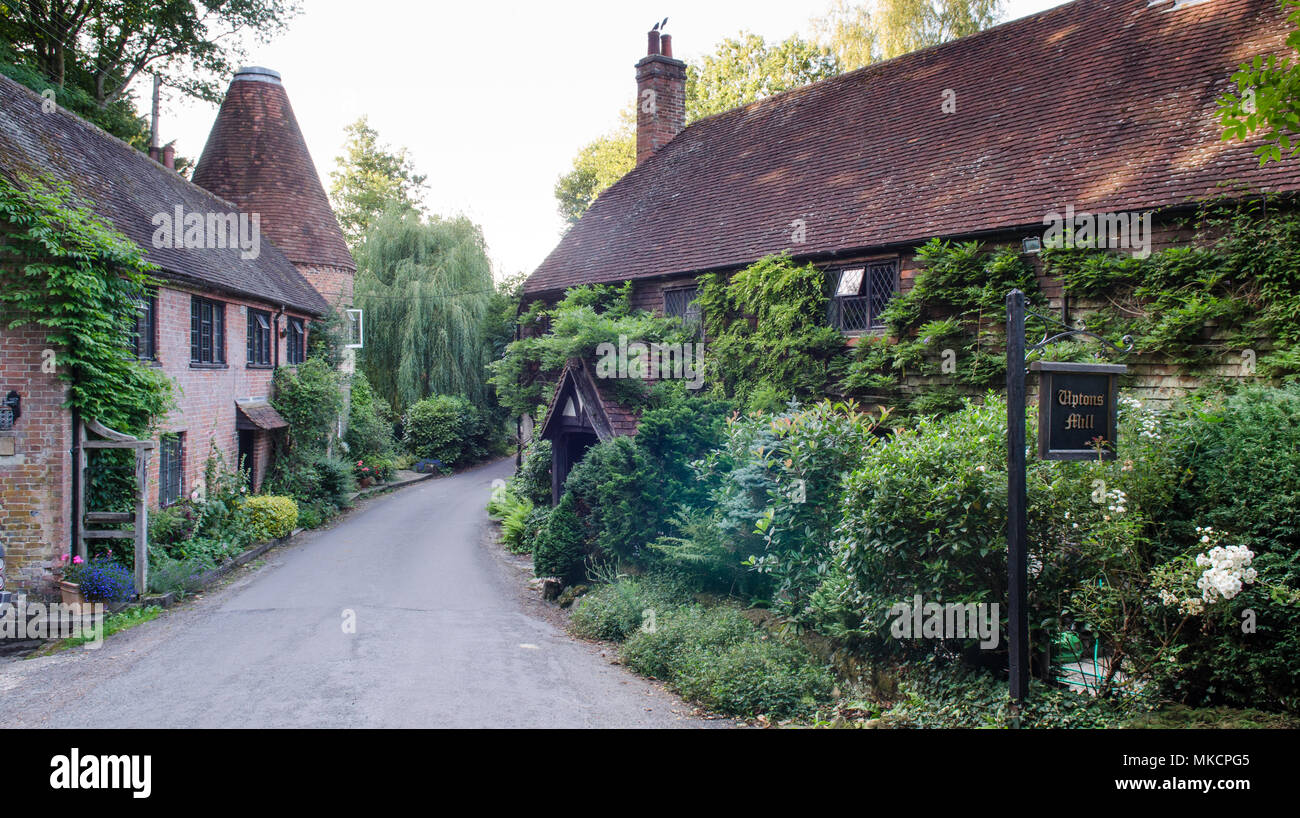 The old plant-covered buildings at Upton's Mill in the Sussex Weald, with the narrow Streele Lane running between them. Stock Photo