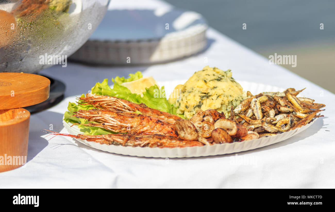 The street food market, seafood served on the paper tray. The green lettuce, calamari, shrimps, small fried fish (grundle/ Grundeln), mashed potatoes. Stock Photo