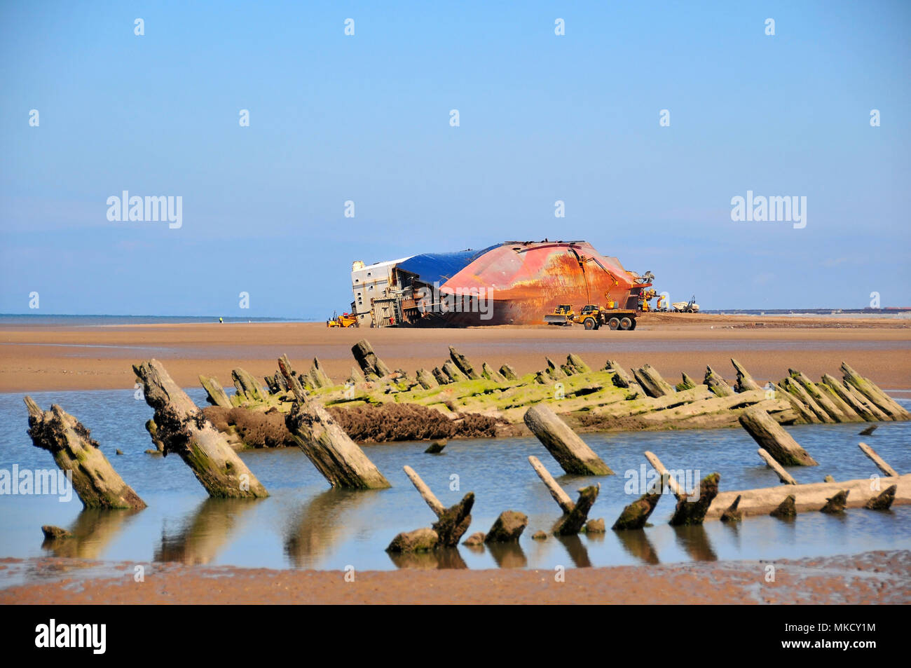 Blue sky view across sand beach of Abana remains in water pool towards Riverdance Ferry wreck on its side, Little Bispham, Blackpool, Lancashire, UK Stock Photo