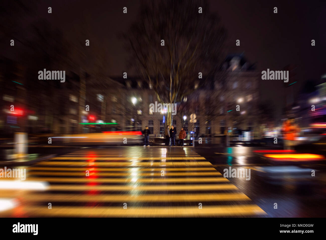 Blurry motion image of people waiting to cross at lights in Republique square at night in Paris. Stock Photo