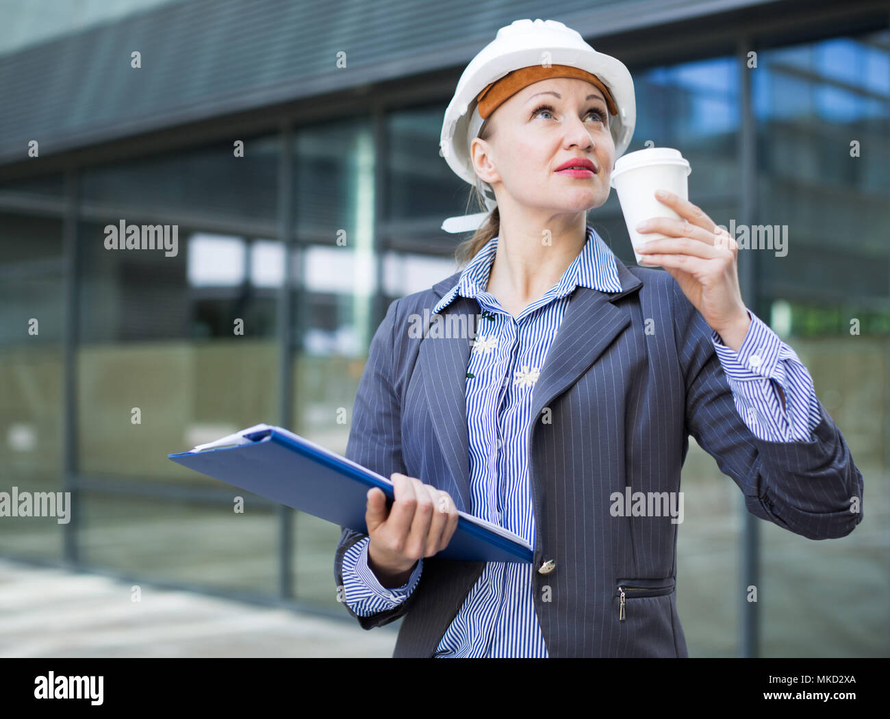 Professional woman in helmet working with documents and drink coffee ...