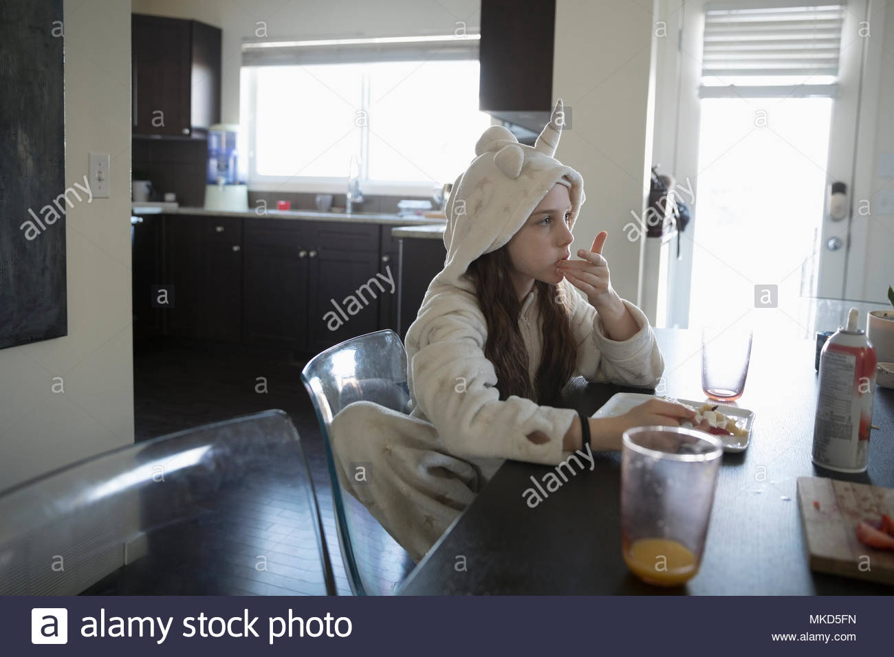 Girl in unicorn pajamas eating breakfast at dining table Stock Photo