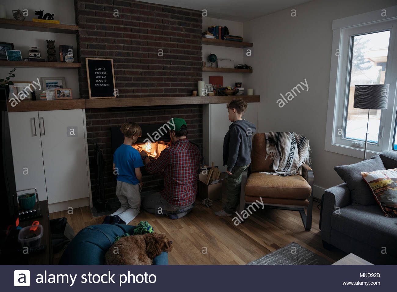 Father And Sons Building Fire In Living Room Fireplace Stock Photo
