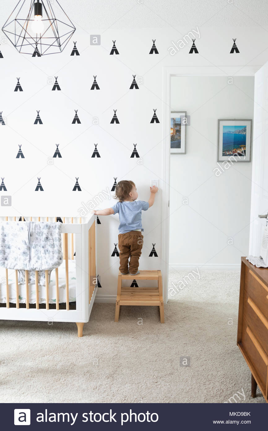 Cute baby boy on step stool reaching for light switch in nursery Stock Photo