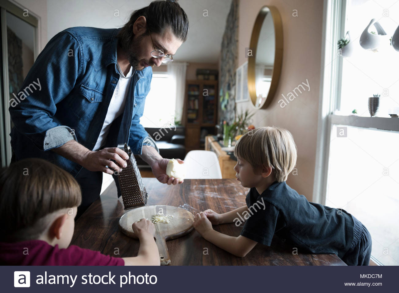 Father and sons grating cheese for homemade pizza at dining table Stock Photo