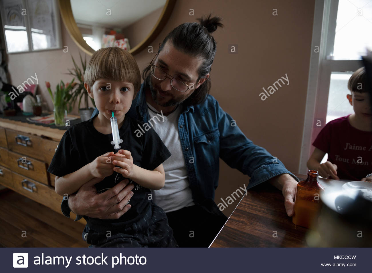 Father giving son medicine at dining table Stock Photo