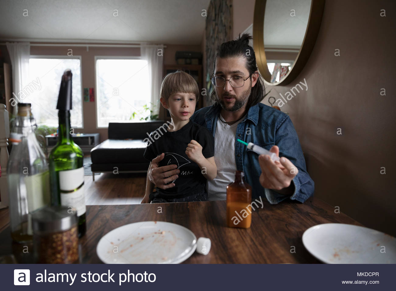 Father giving son medicine at dining table Stock Photo