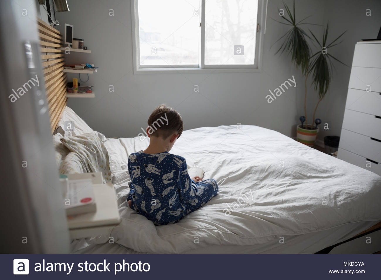 Boy in pajamas reading book on bed Stock Photo