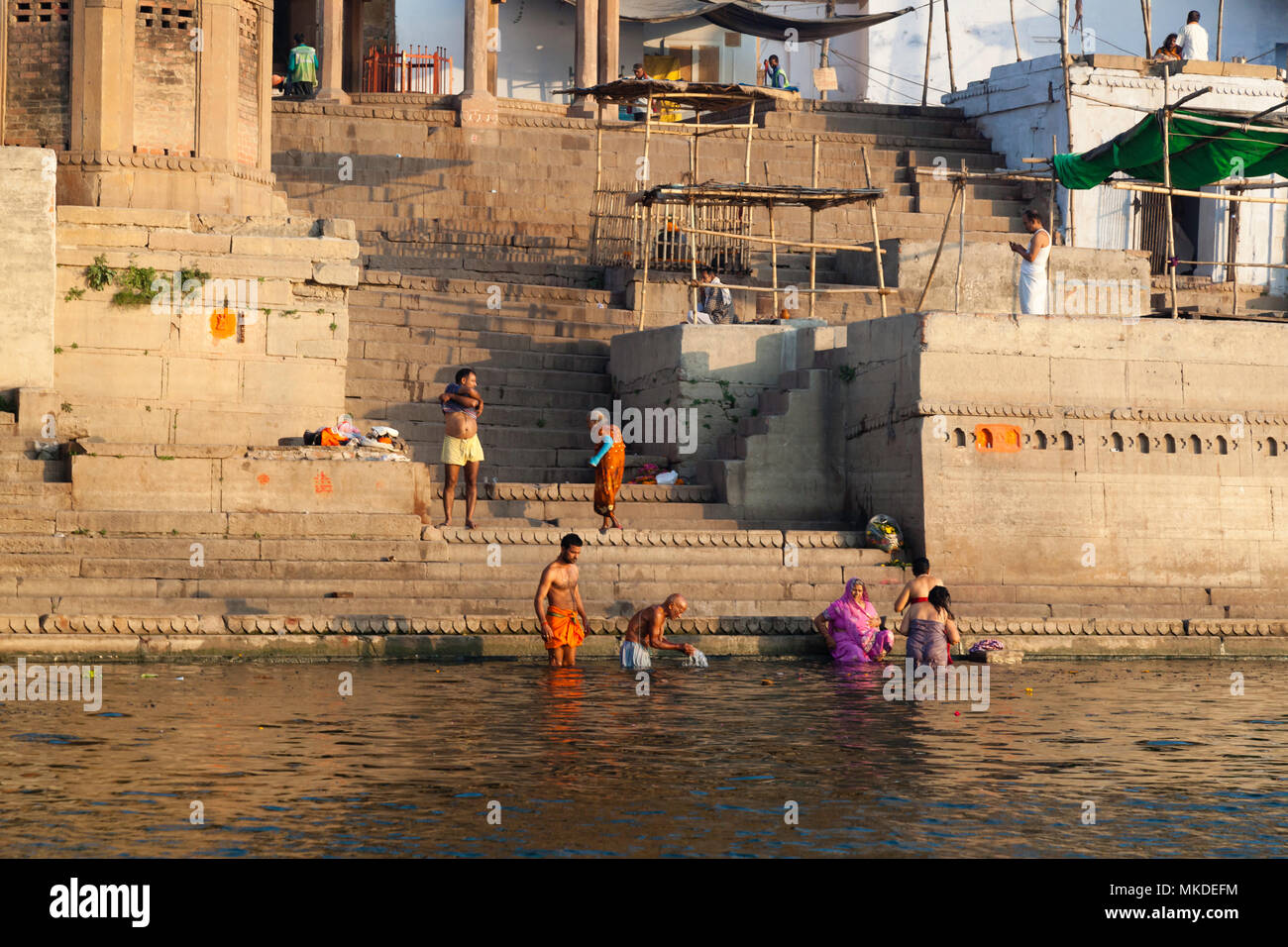 A Hindu family wash away their sins in the river Ganges whilst others offer prayers to their Gods from the Ghats of Varanasi. Stock Photo