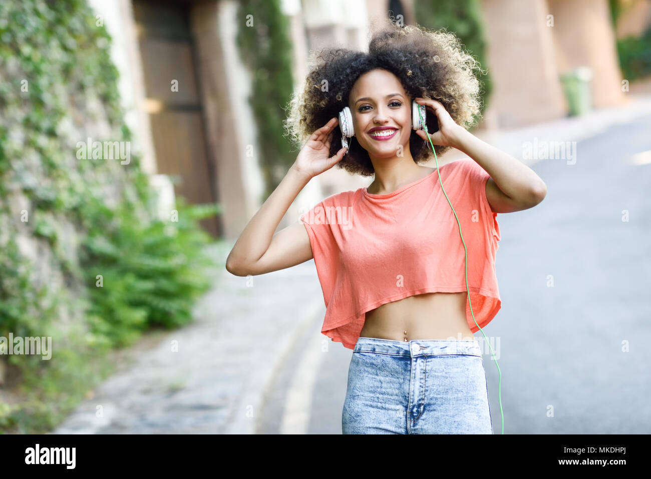 Portrait of young attractive black girl in urban background listening to  the music with headphones. Woman wearing orange t-shirt and blue jeans with  a Stock Photo - Alamy