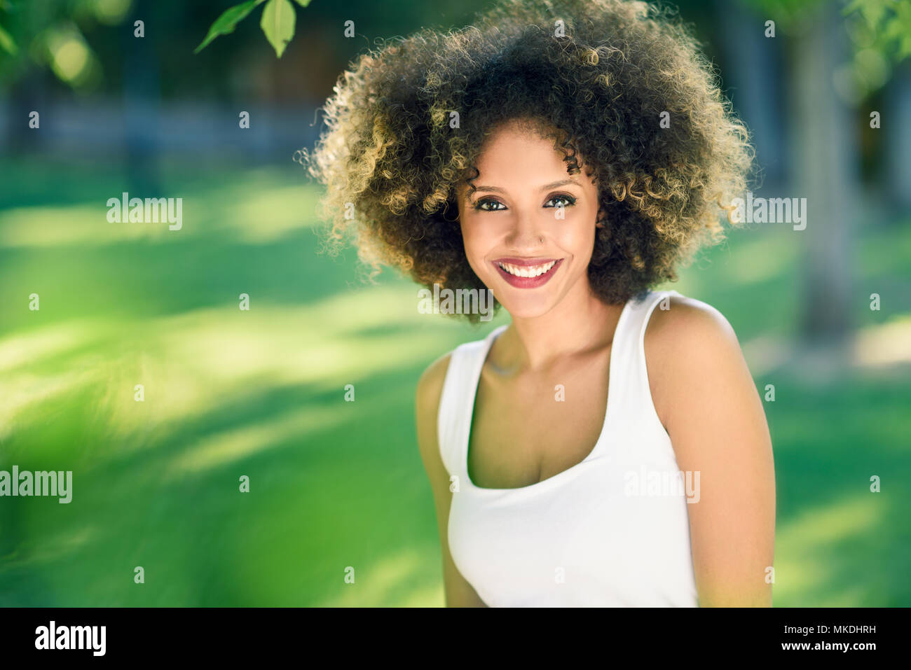 Young black woman with afro hairstyle smiling in urban park. Mixed girl ...