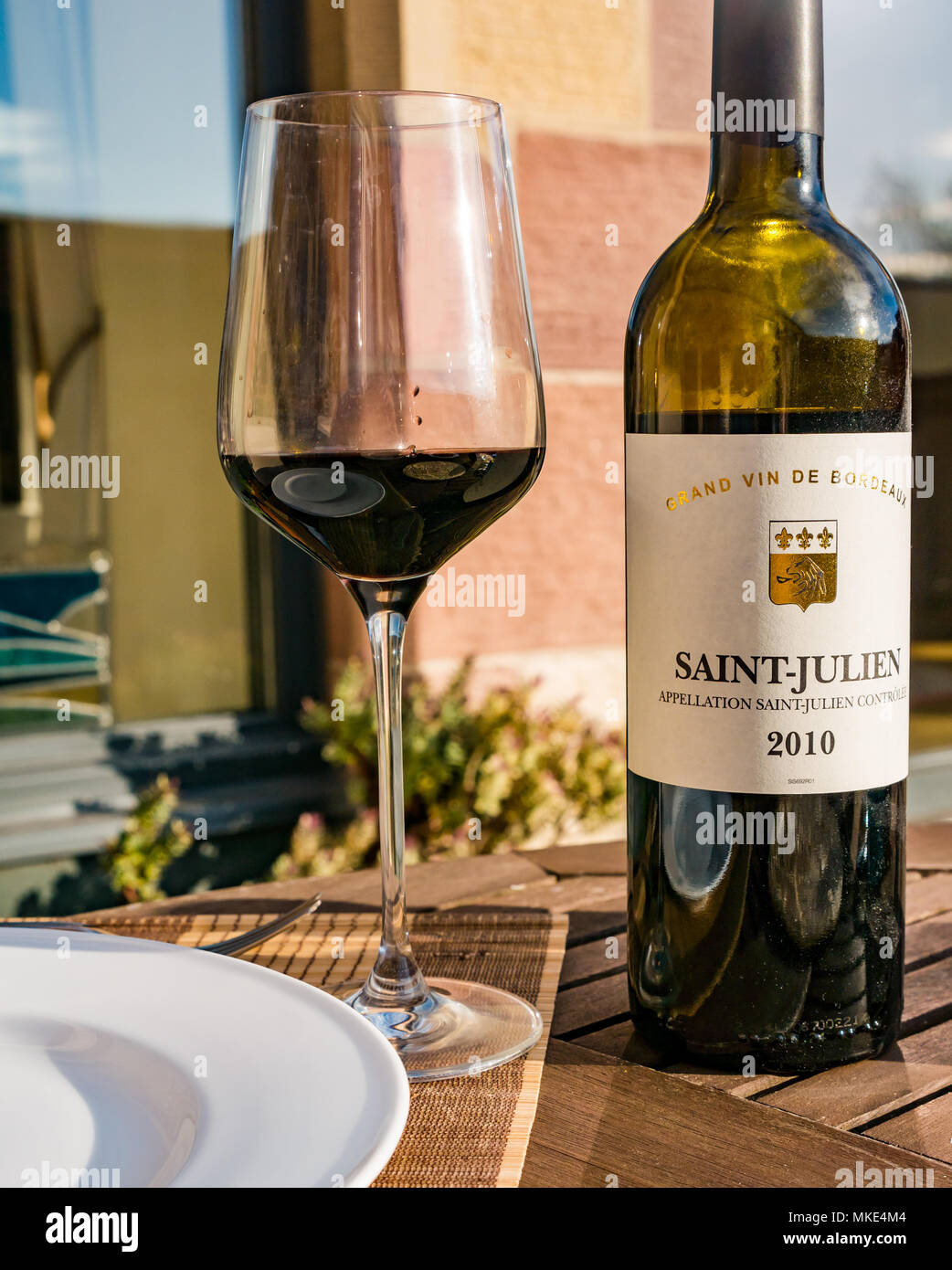 Close up sunlit red wine claret bottle and wine glass on outdoor patio table, Saint-Julien, Grand Vin de Bordeaux Stock Photo