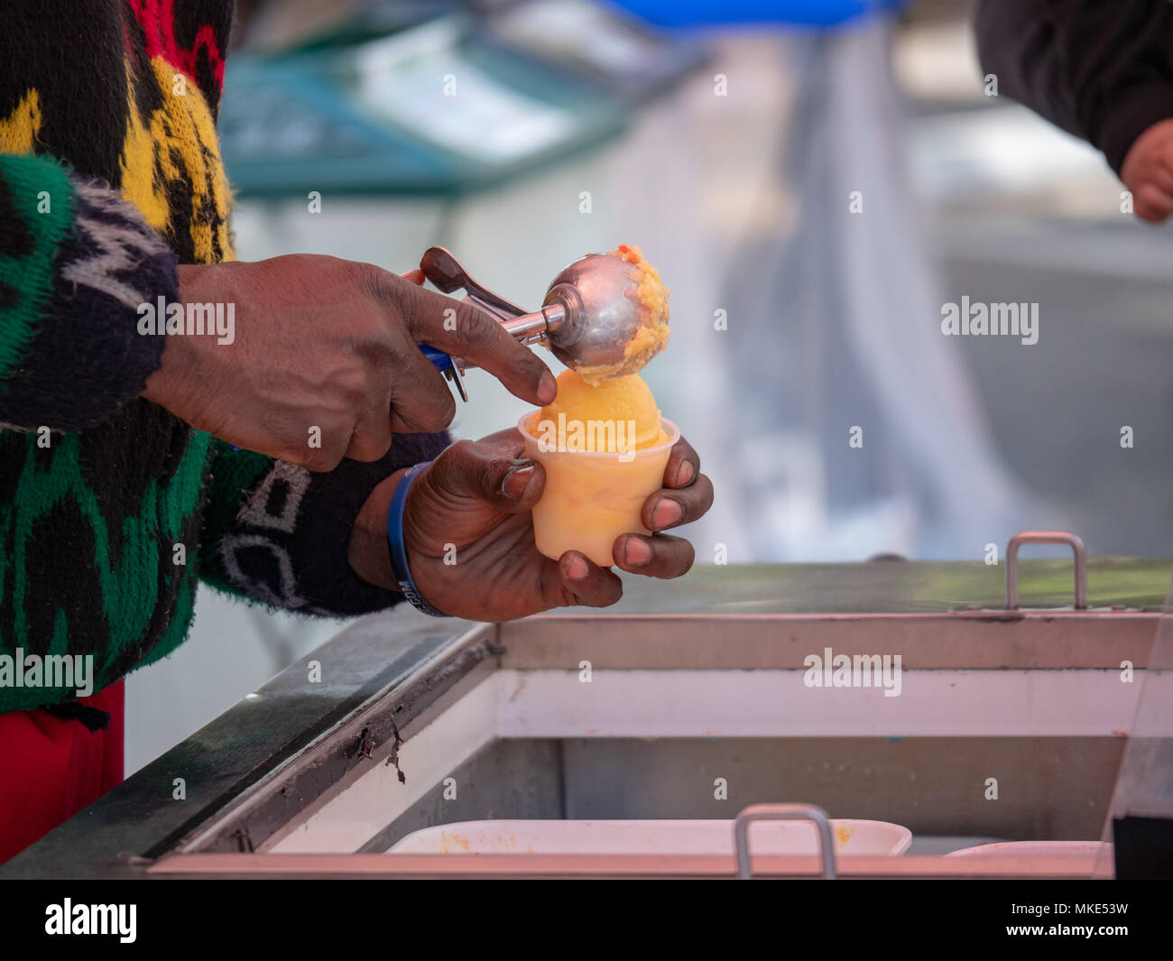 Server scoops orange flavored Italian ice into cup Stock Photo