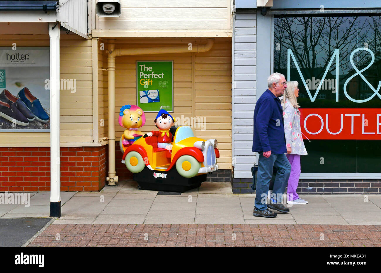 Middle aged couple in casual dress walking past childrens' Noddy Car ride Stock Photo