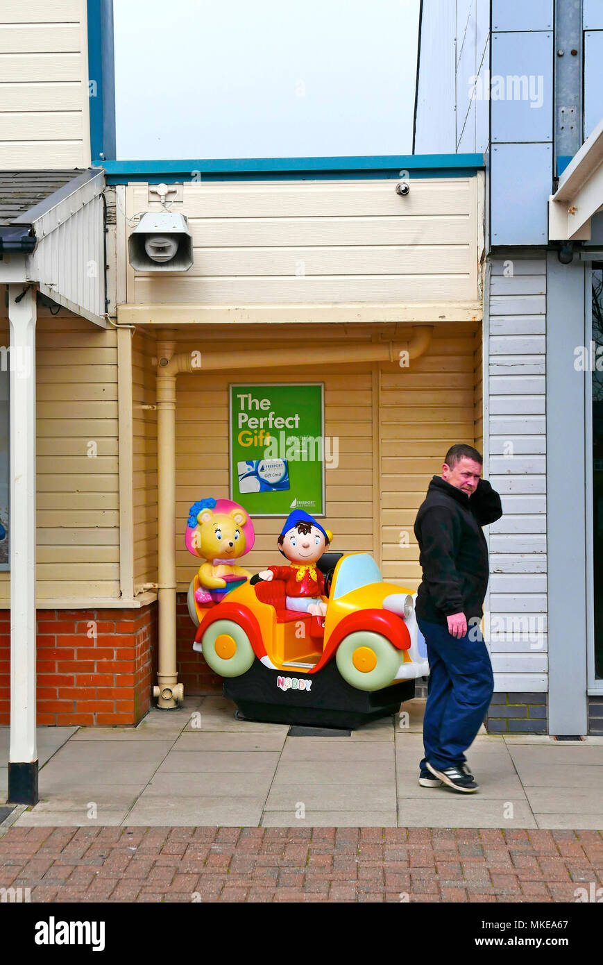 Man in casual dress walking past childrens' Noddy Car ride Stock Photo