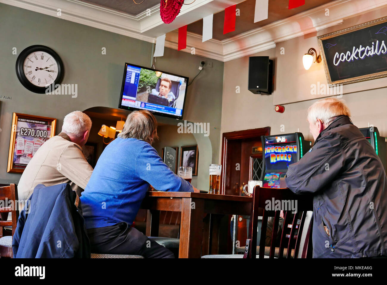 Three senior men sat in pub drinking beer and watching television Stock Photo