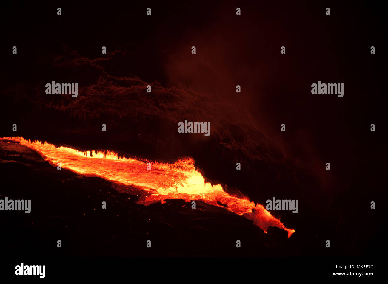 A fiery lava flows from the crack of the El-Afar volcano and flows down the mountain slope, a night photograph, North Ethiopia. Stock Photo