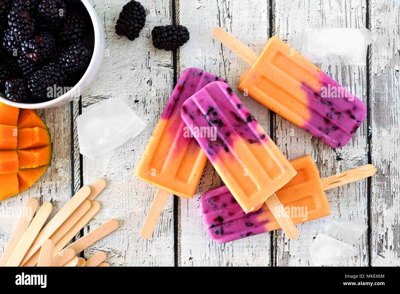Group of homemade mango blackberry popsicles, top view on a rustic white wood background Stock Photo