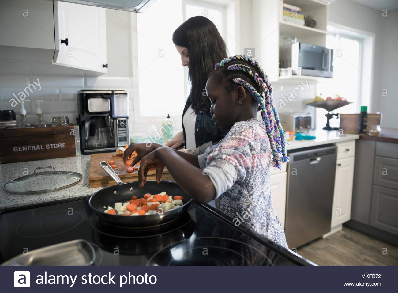 Mother and daughter preparing and cooking vegetables at kitchen stove Stock Photo