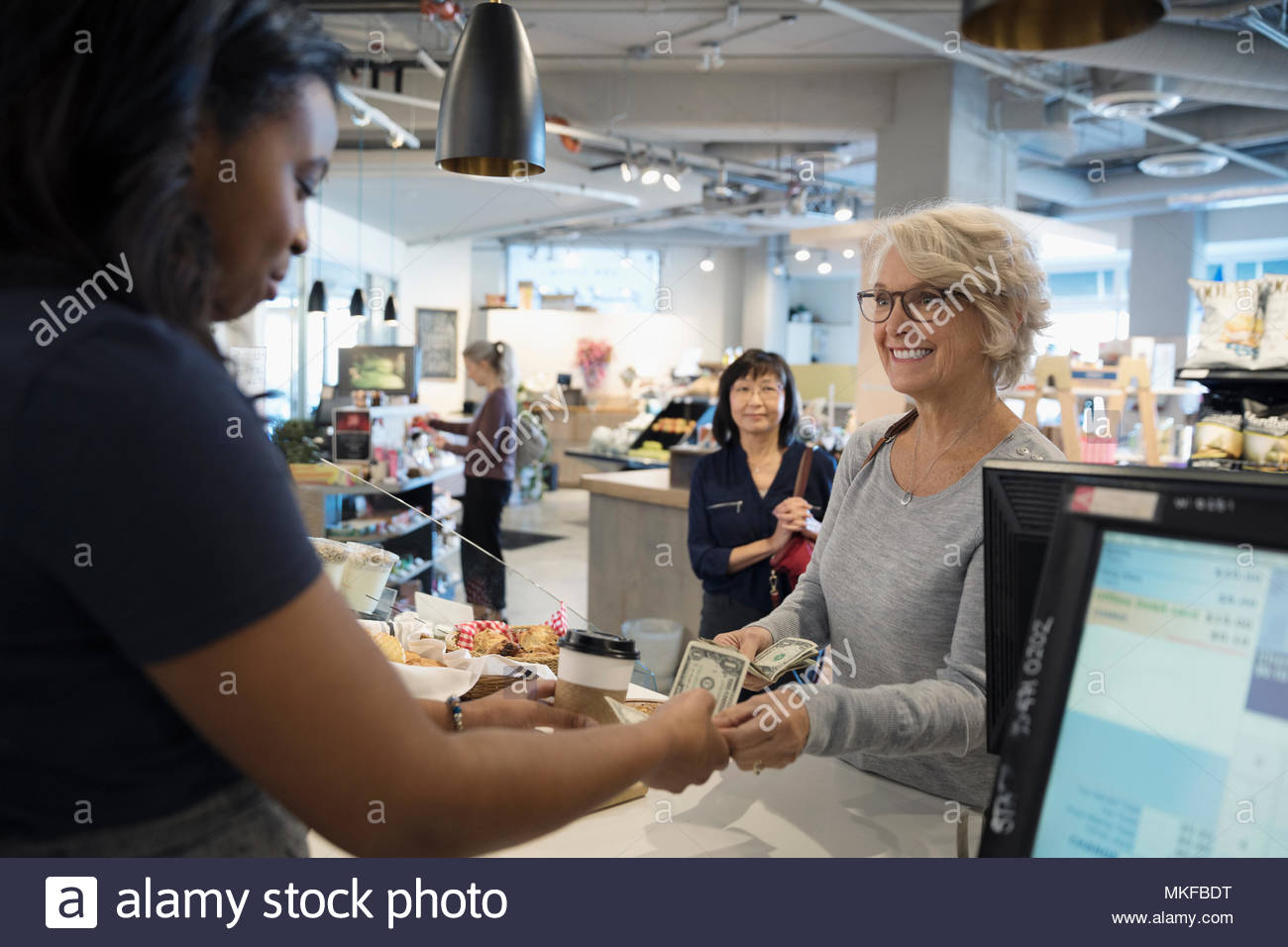 Smiling senior woman paying worker with cash at market checkout Stock Photo