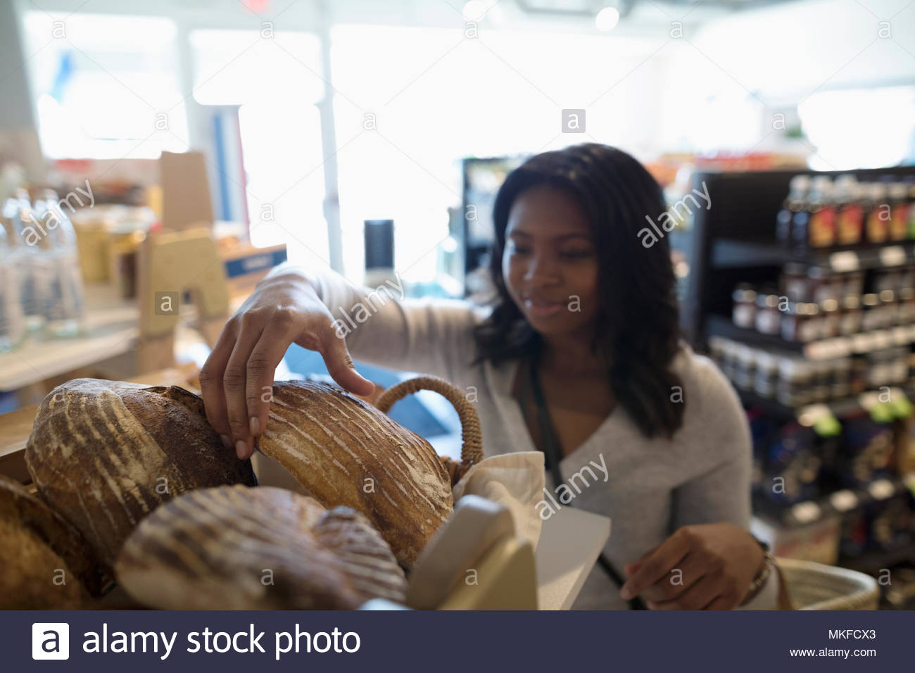 Young woman grocery shopping, reaching for fresh bread in market Stock Photo