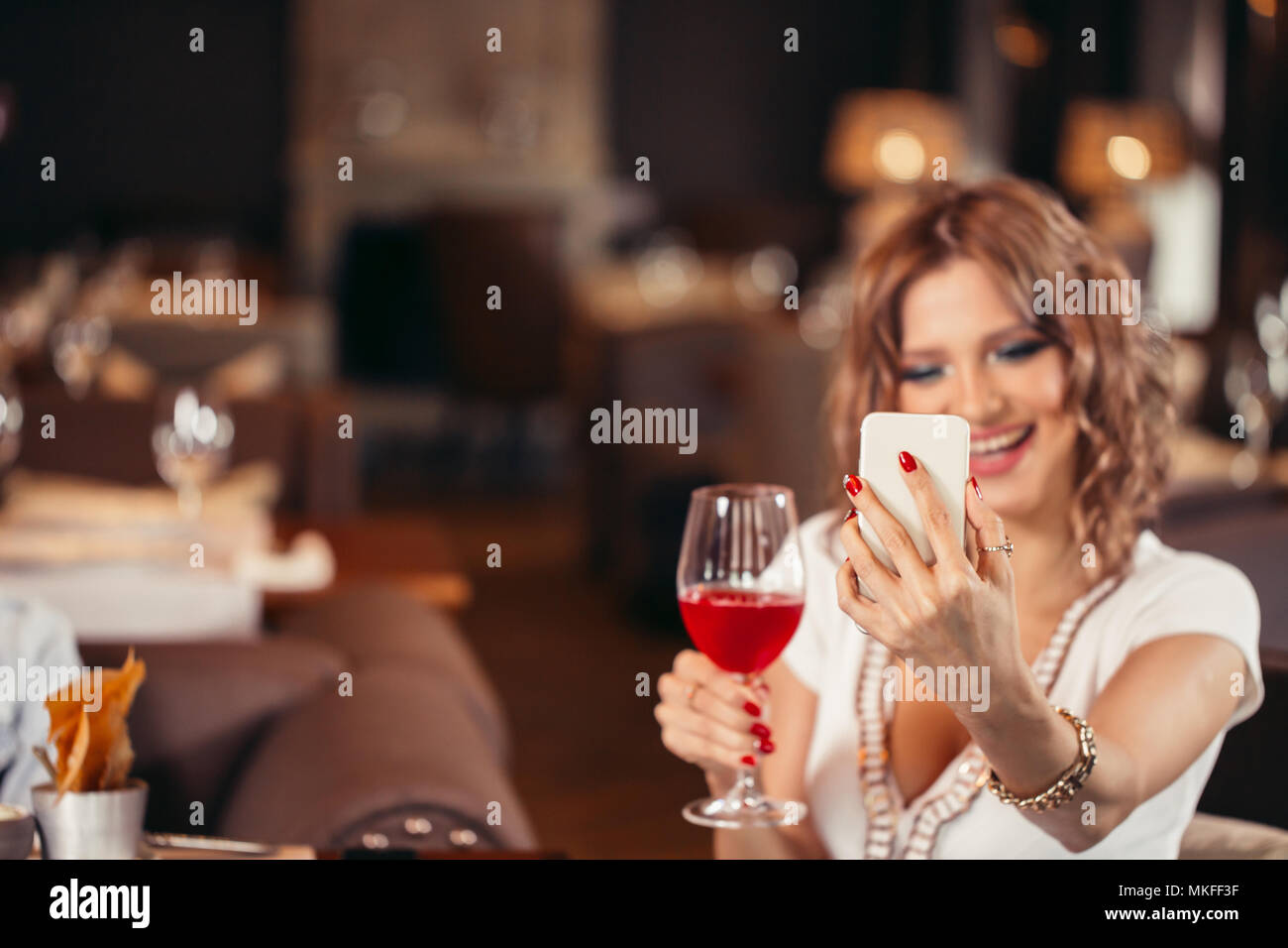 https://c8.alamy.com/comp/MKFF3F/young-happy-white-woman-with-a-glass-of-wine-taking-selfie-at-restaurant-MKFF3F.jpg