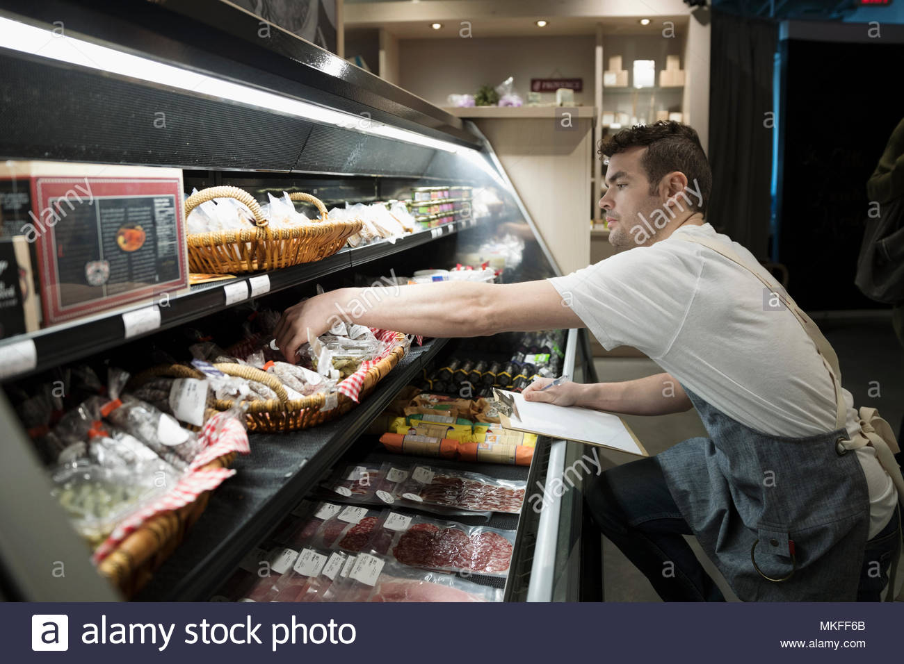 Male worker with clipboard taking inventory at deli case in grocery