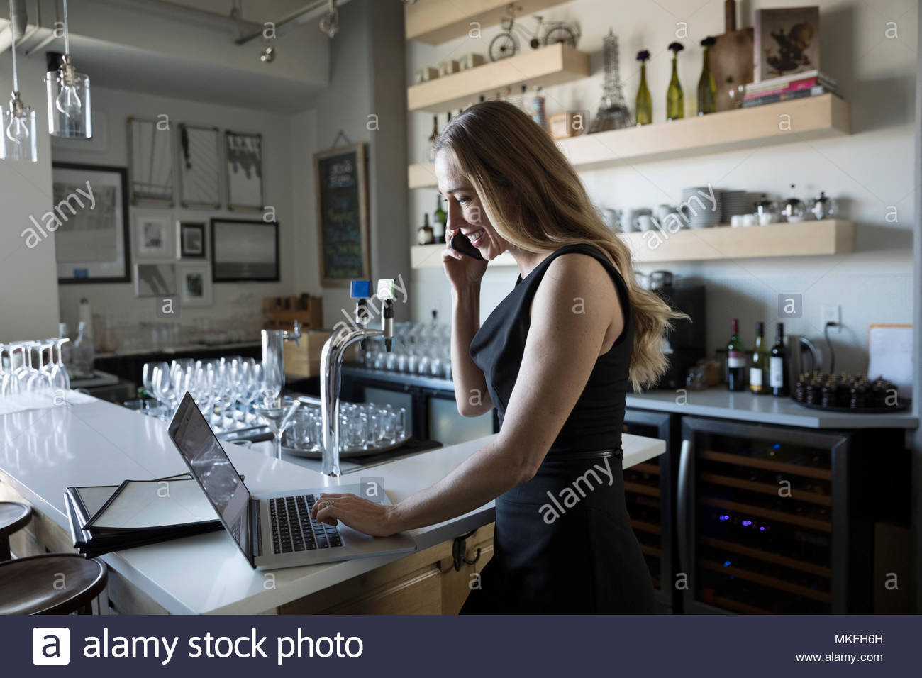 Female small business owner talking on smart phone and working at laptop in cafe Stock Photo