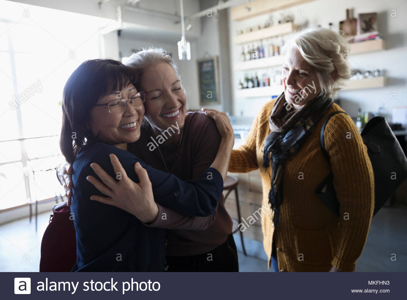 Happy senior women friends greeting, hugging in cafe Stock Photo