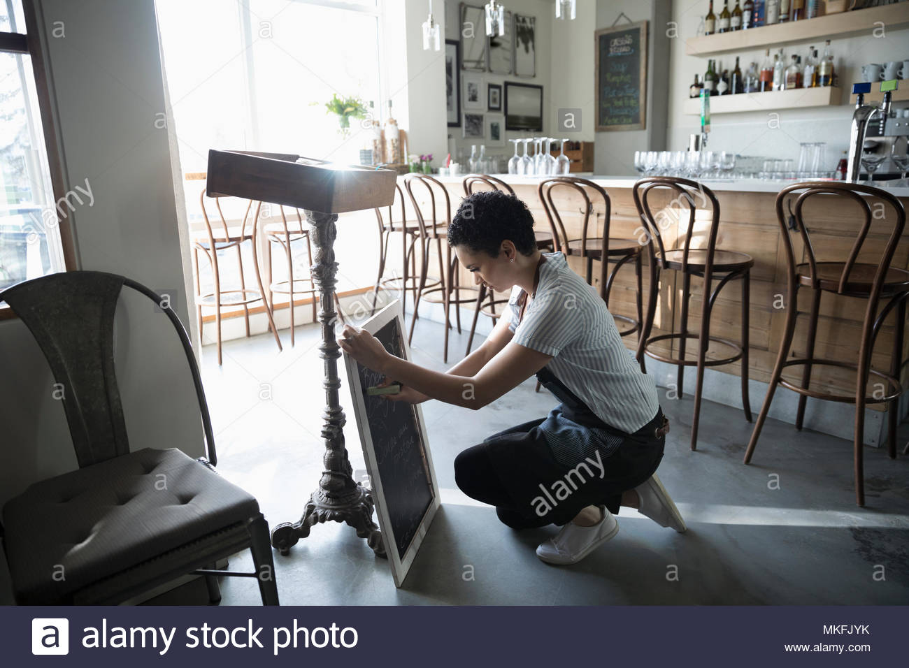 Young woman small business owner preparing menu on cafe blackboard Stock Photo
