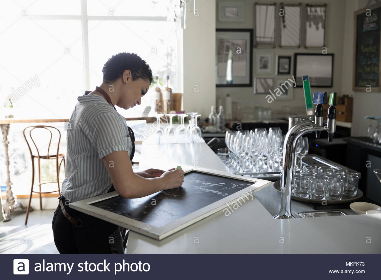 Young woman small business owner preparing menu on cafe blackboard Stock Photo