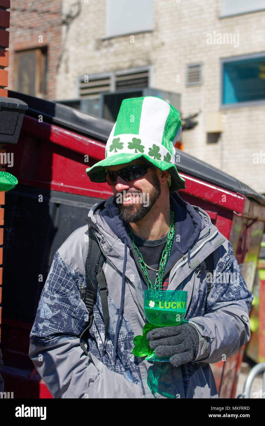 A spectator at the Montreal St Patrick's Day parade wearing a green hat and drinking beer from a green glass Stock Photo