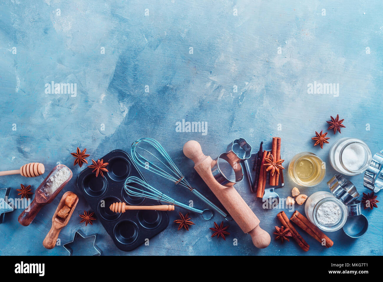 Making pastry concept with baking tools and ingredients on a modern concrete background with copy space. Wooden scoops, whisks, cookie cutters, muffin tin, sugar, flour, anise stars from above. Stock Photo