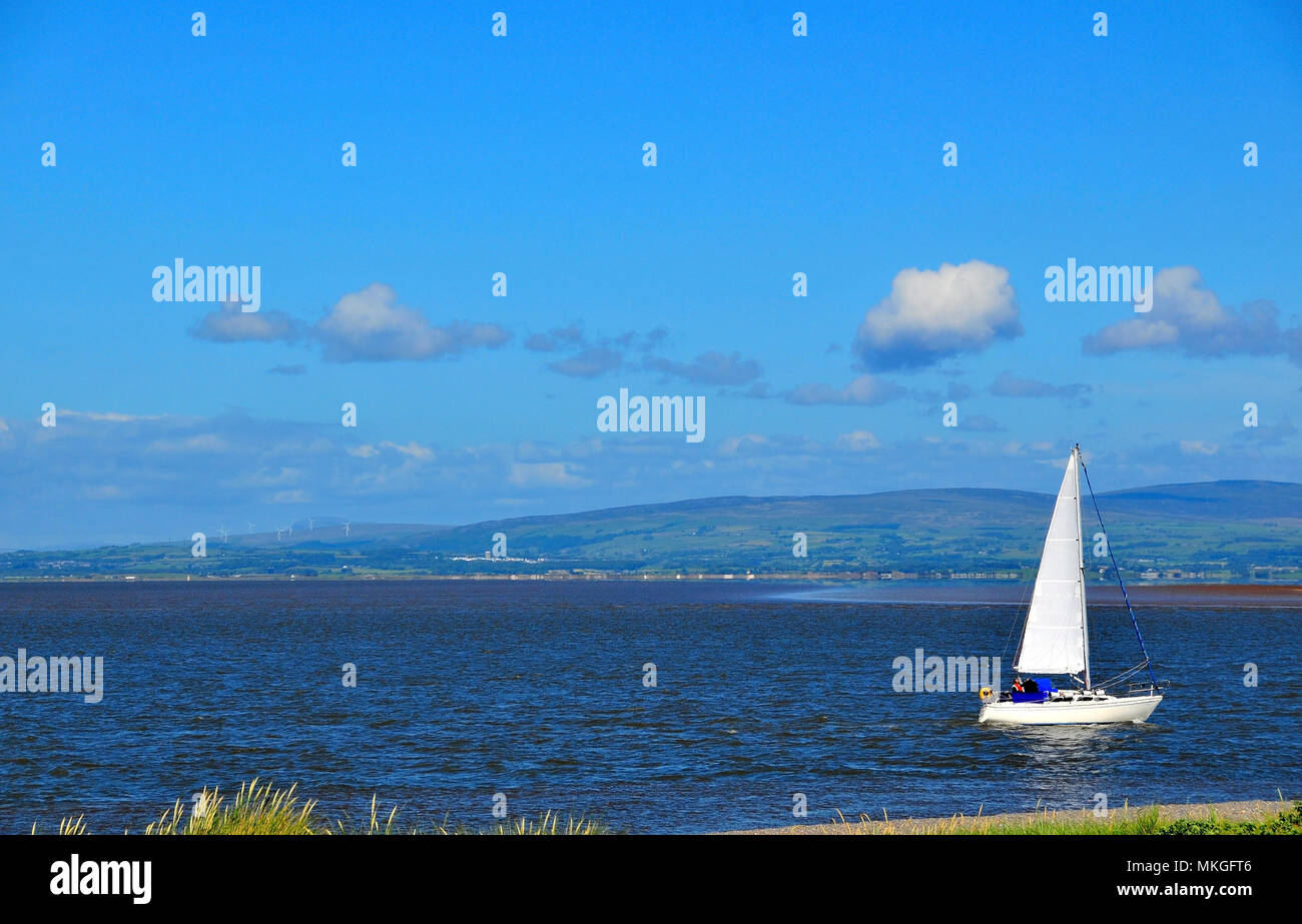 Sunny view of white yacht moving over calm sea water, from coastal footpath east of Kott End, Lancashire, UK Stock Photo