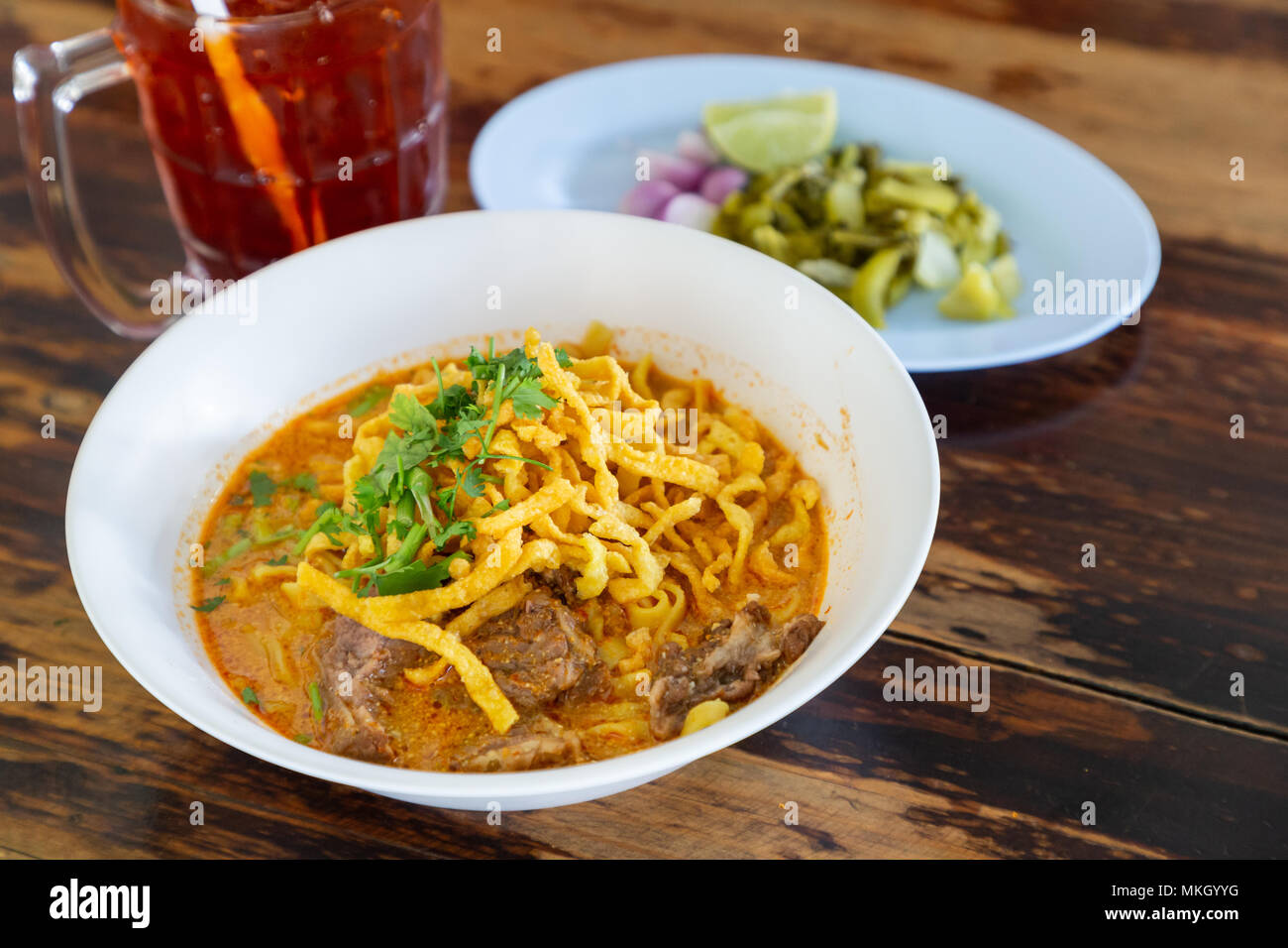 Curried noodle soup (Khao soi) with beef and spicy coconut milk on wood table. Thai food cuisine