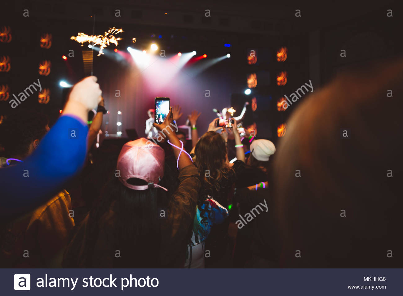 Milennials with smart phones in crowd videoing musicians performing in nightclub Stock Photo