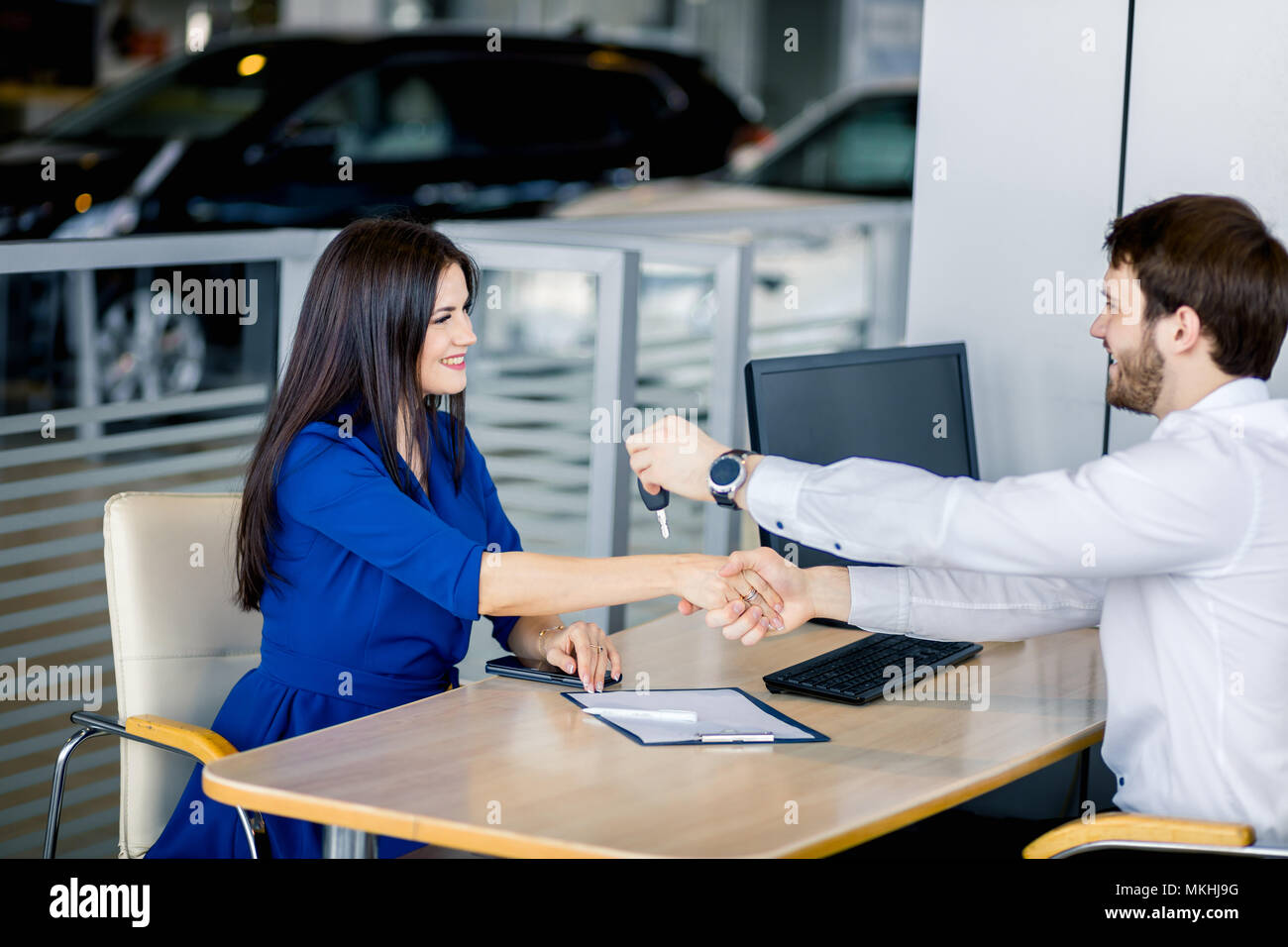Man shaking her girlfriends hand with one hand, congratulating on a new car while giving key by onother hand at auto salon Stock Photo