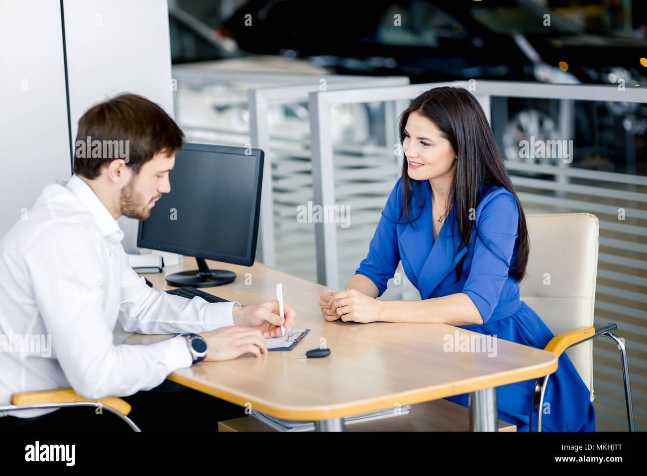 Young caucasian couple writing out all advantages of buying a new car in the dealer office Stock Photo
